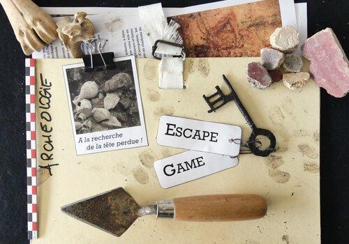 Visuel d'un dossier comportant une vieille photo d'un chantier archéologique et divers outils ou objet de fouille. On peut lire dessus "A la recherche de la tête perdue" et "Escape Game".