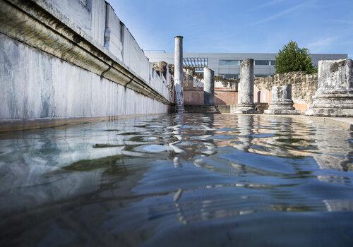 bassin semi-circulaire rempli d'eau ou se reflètent les murs et colonnes romaines