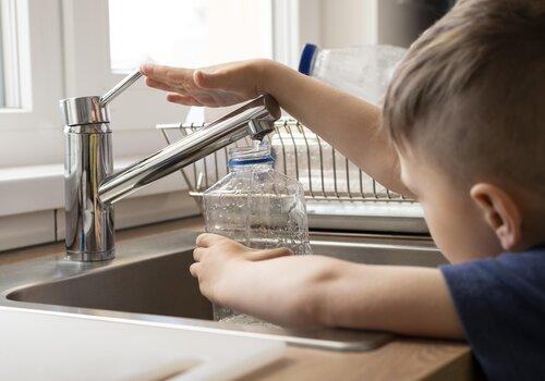 Enfant remplissant une bouteille en plastique au robinet