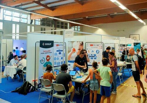 Sur un stand du village des sciences de montpellier, deux femmes présentent à des enfants et une adulte des documents sur l'étude des sons et de l'audition humaine