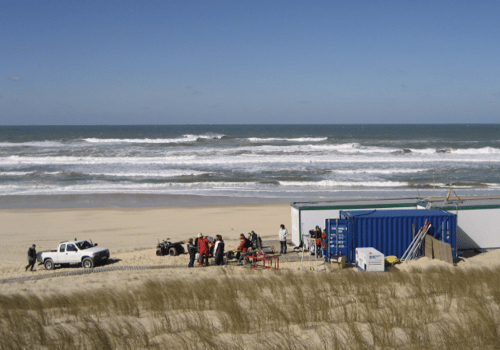 Vue d'une plage et de la mer en fond. Une équipe scientifique en premier plan.