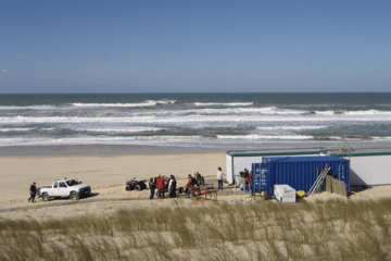 Vue d'une plage et de la mer en fond. Une équipe scientifique en premier plan.